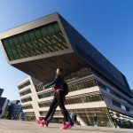 WU-Campus Wien mit Blick von unten auf das Learning Center von Zaha Hadid mit zwei vorbeigehende Personen. Ein Bild von MANFRED SODIA photography.